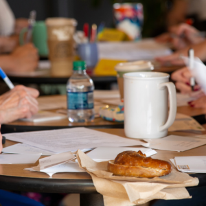 Writers at a table with pens and paper and coffee cup and water bottle and pastry